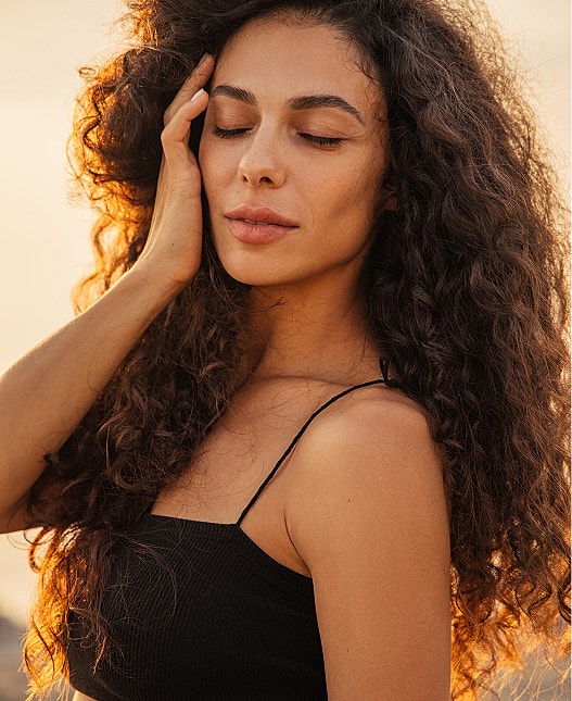 Woman with curly hair in sunset light.