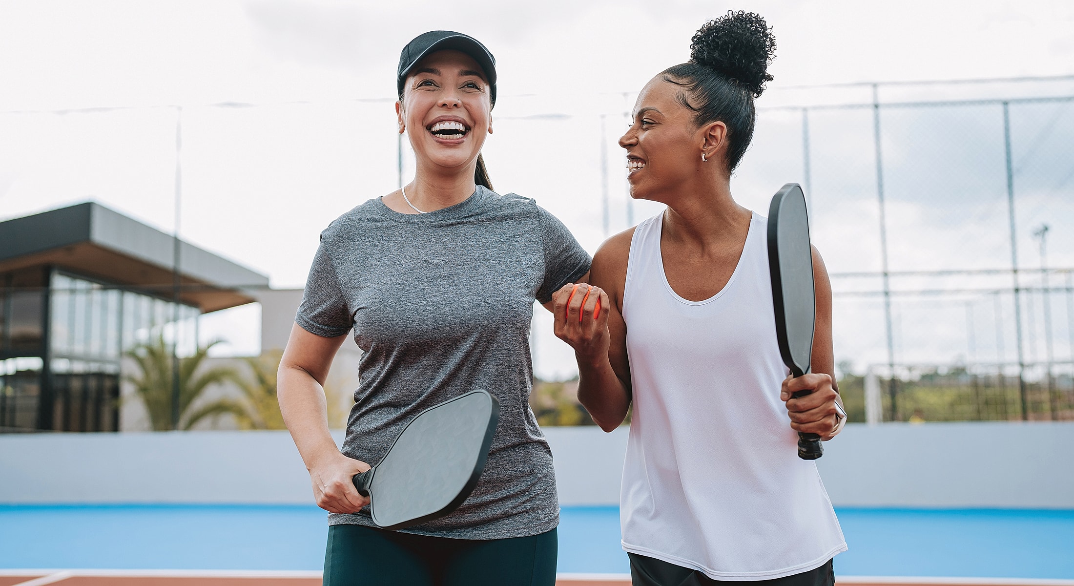 Smiling friends chatting with pickleball paddles.